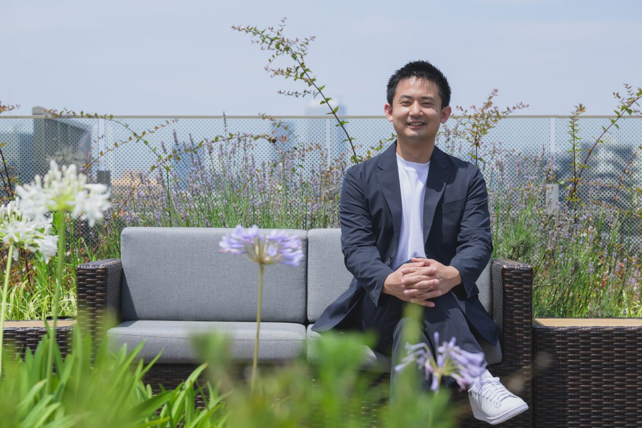 屋上のソファに座り、穏やかにほほえむ代表の藤原亮太